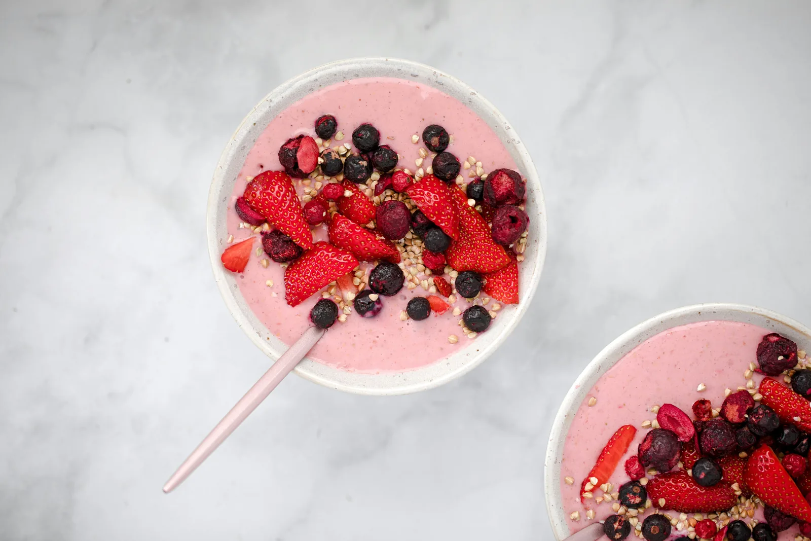 A bowl of berry smoothie topped with fresh strawberries and blueberries